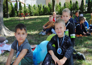 chłopcy z medalami na szyi siedzą w cieniu drzew